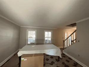 Interior room with freshly painted walls, crown molding, and protective floor coverings during painting project