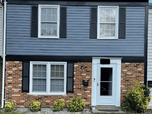 Blue painted siding with white trim, shutters, and door on brick lower level