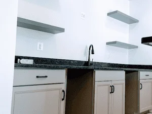 White painted kitchen cabinets with black hardware, floating shelves, and granite countertop
