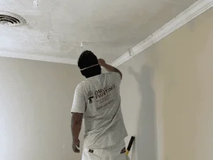 Worker performing drywall taping and mudding on ceiling with joint compound