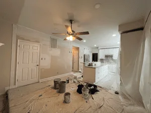 Interior room with drywall preparation, drop cloths, and masked fixtures ready for painting