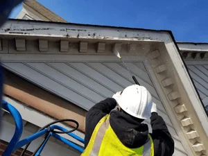Painter in safety gear applying paint to residential soffit and fascia trim